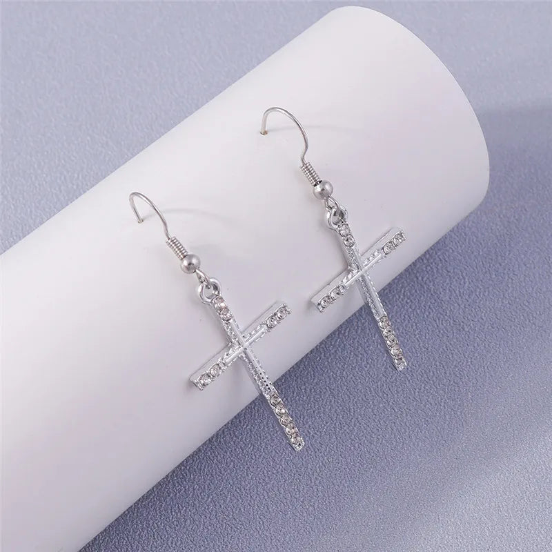 Silver cross-shaped earrings on a white cylindrical object with a light purple background