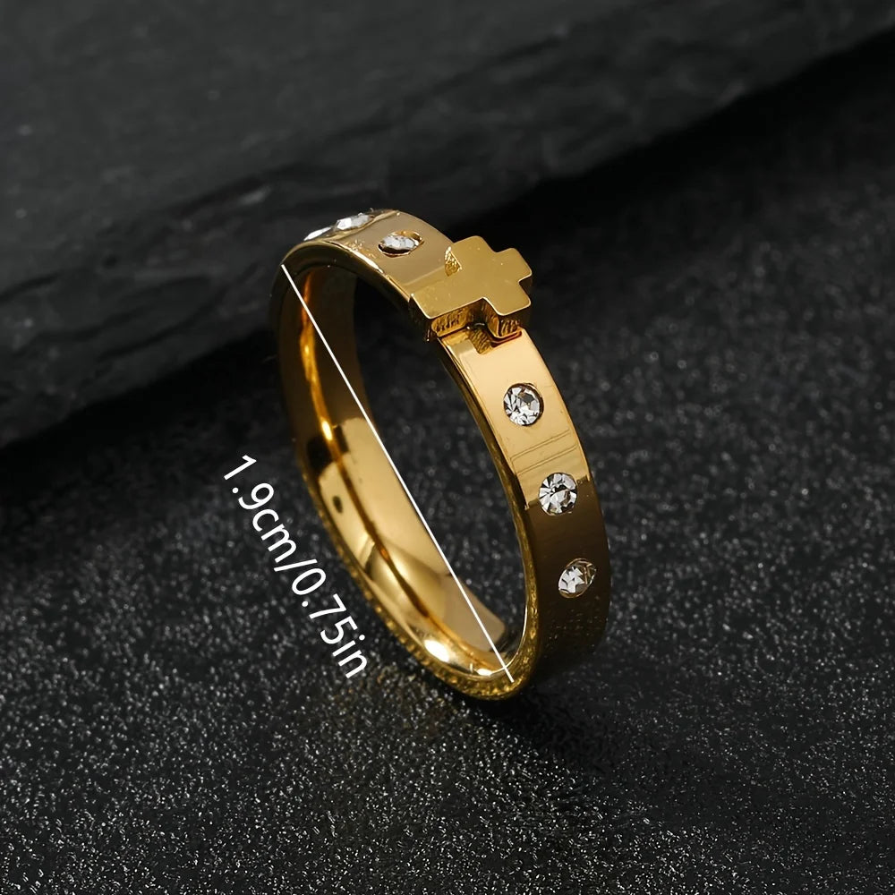 Gold ring with cross design and gemstones on a dark surface
