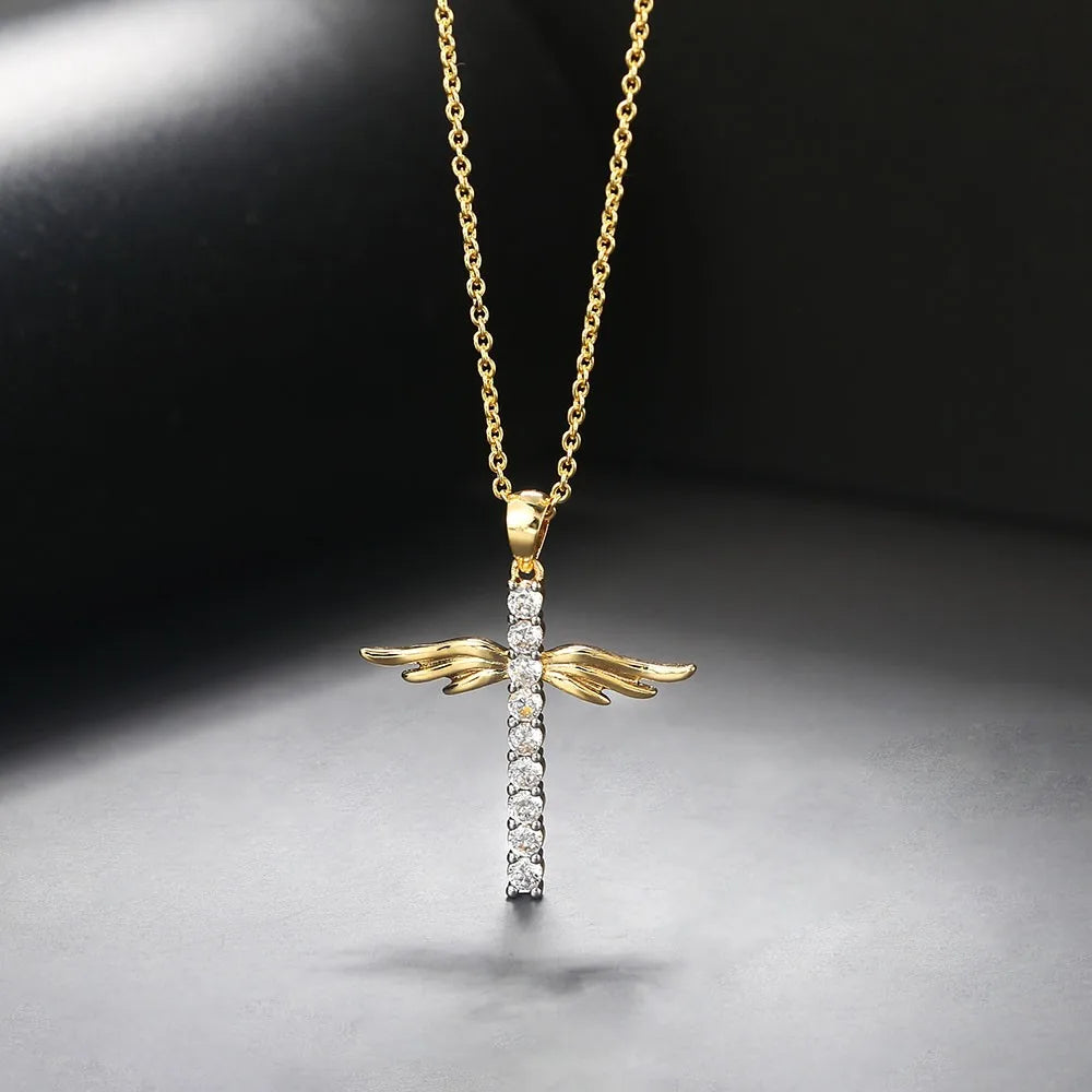 Gold cross pendant with wings on a chain against a dark background