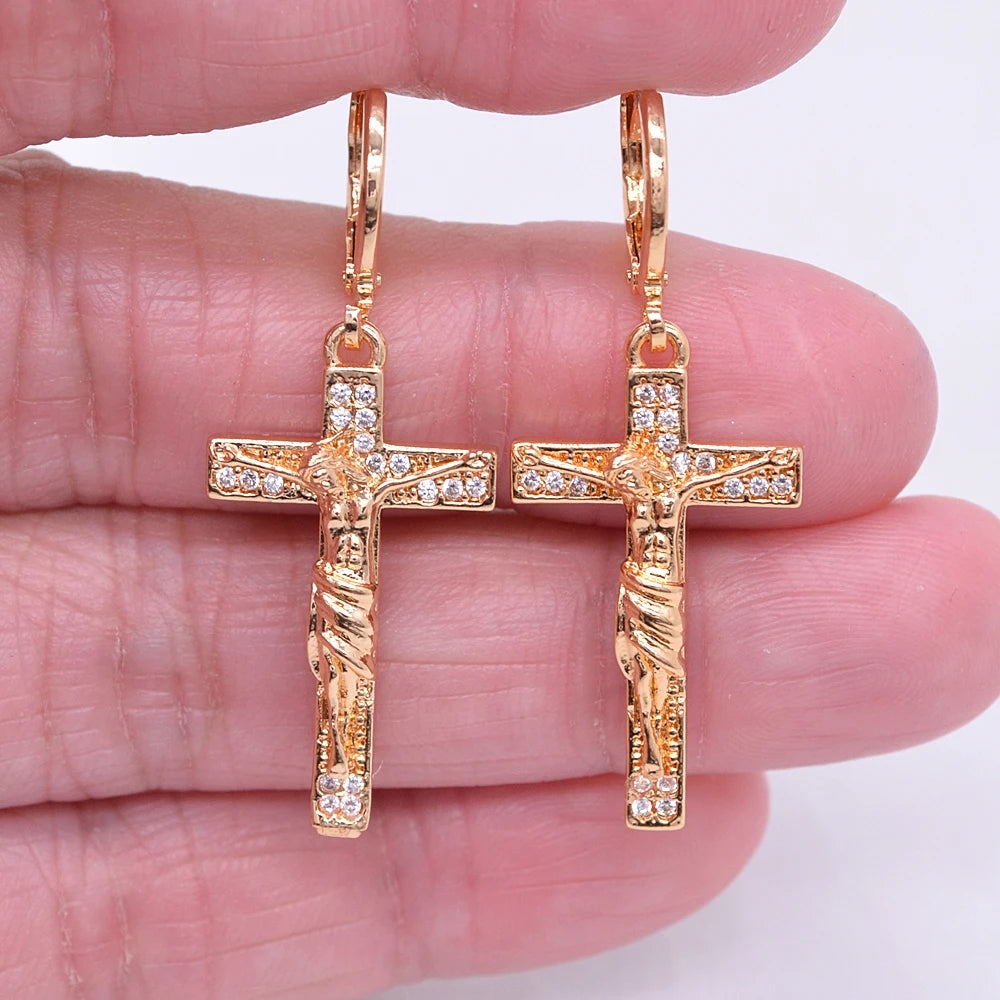 Rose gold cross earrings with Jesus Christ design held between fingers on a white background