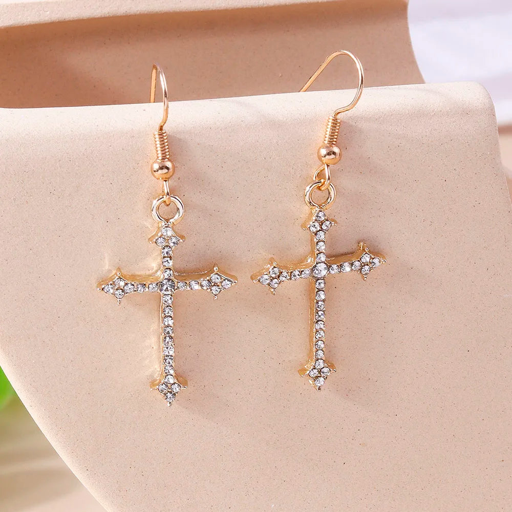 Gold cross earrings with clear stones on a beige stand