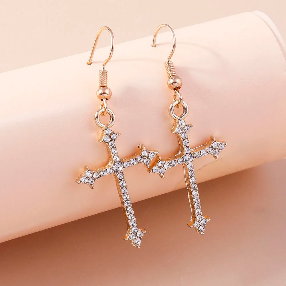 Gold cross earrings with clear stones on a beige background