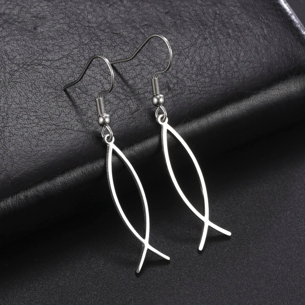 Silver fish-shaped earrings on a dark textured surface