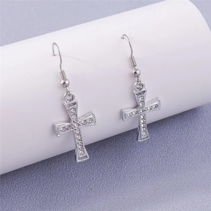Silver cross earrings on a white cylindrical object with a gray background