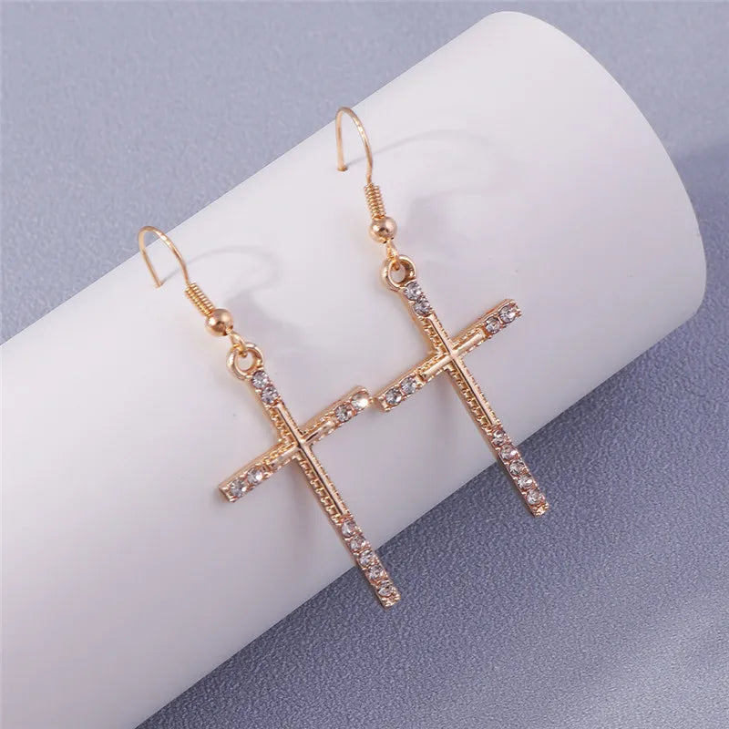 Gold cross-shaped earrings with rhinestones on a white surface
