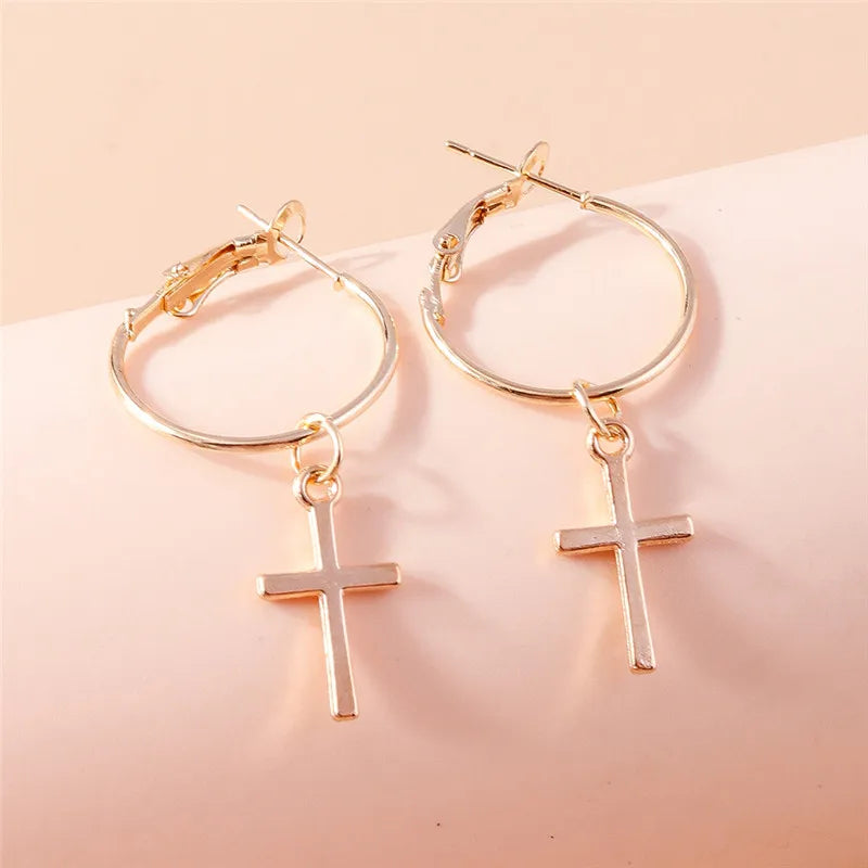 Gold hoop earrings with cross pendants on a light pink background