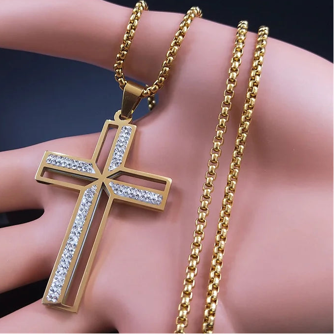 Gold cross pendant with chain on a hand against a dark background