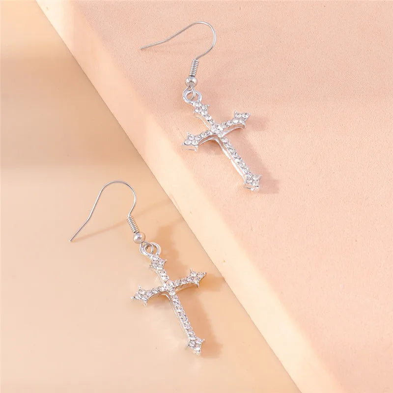 Silver cross-shaped earrings on a beige background