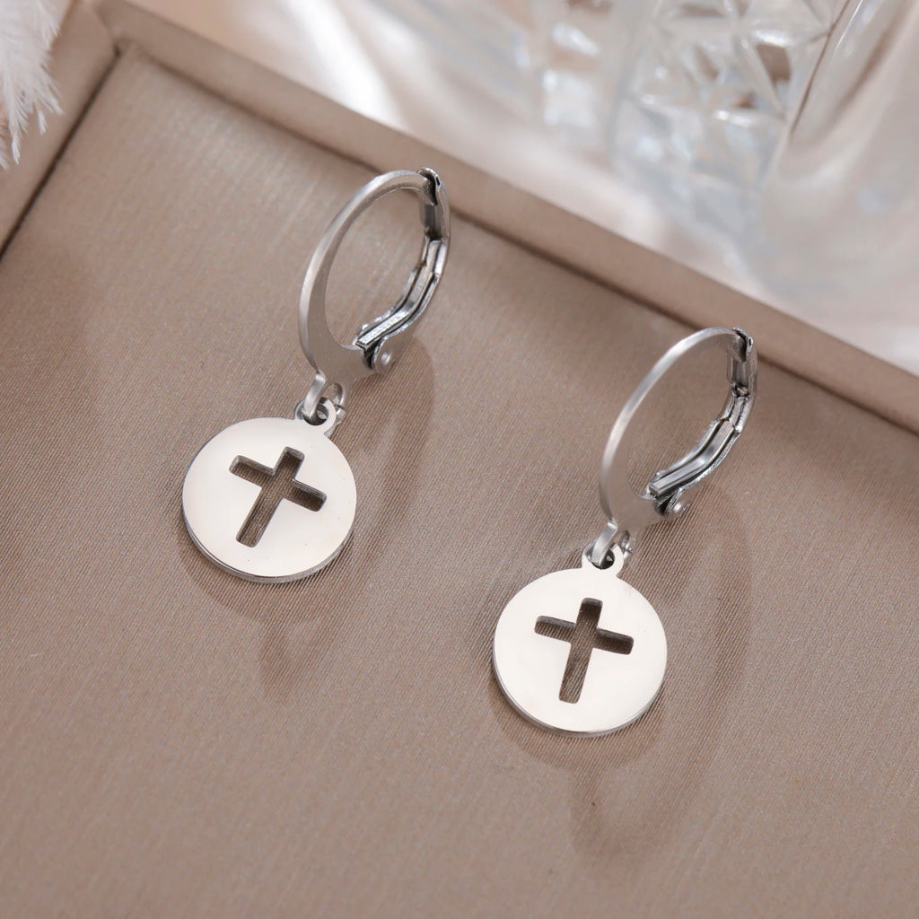 Silver hoop earrings with round disc charms featuring crosses on a beige surface.