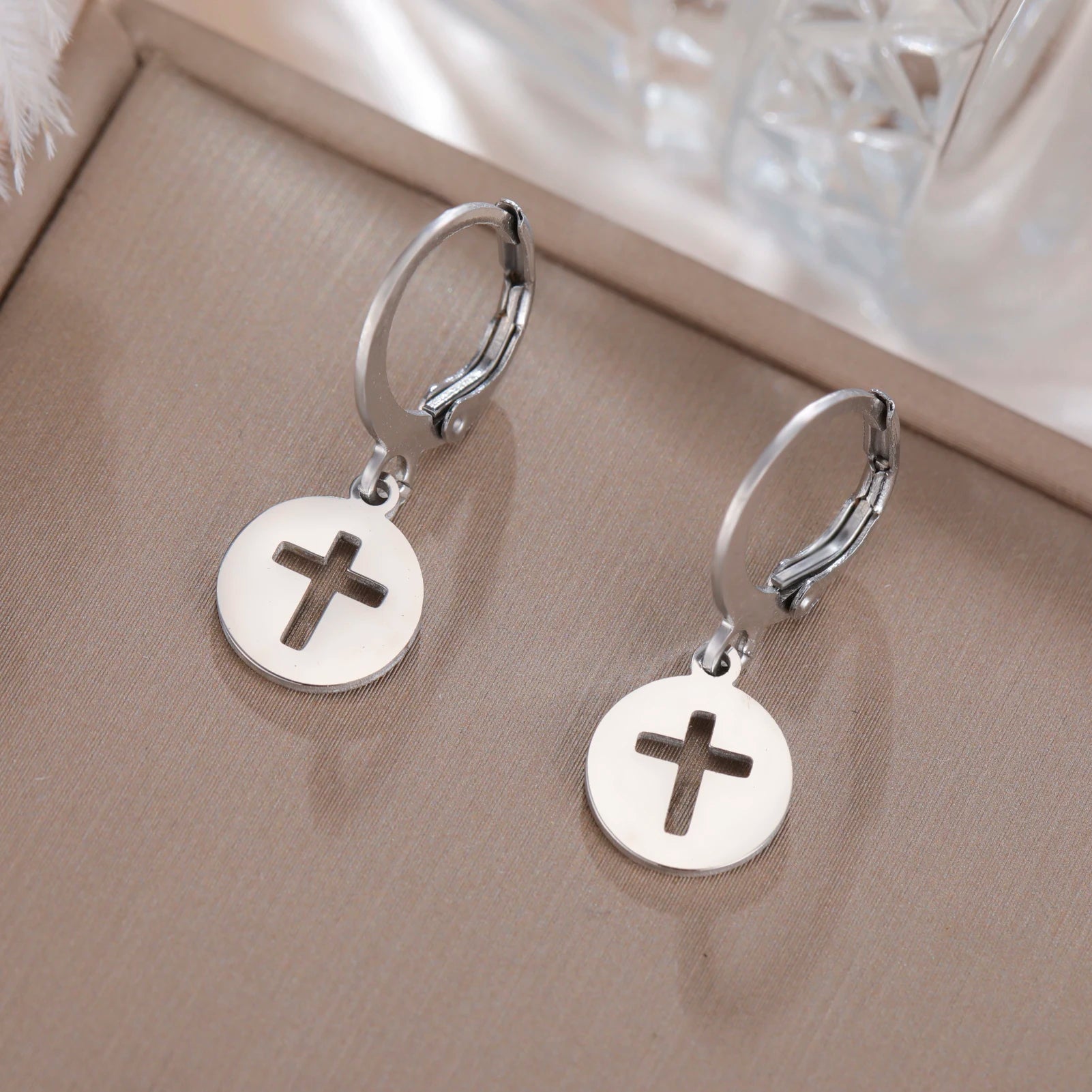 Silver hoop earrings with round disc charms featuring crosses on a beige surface.