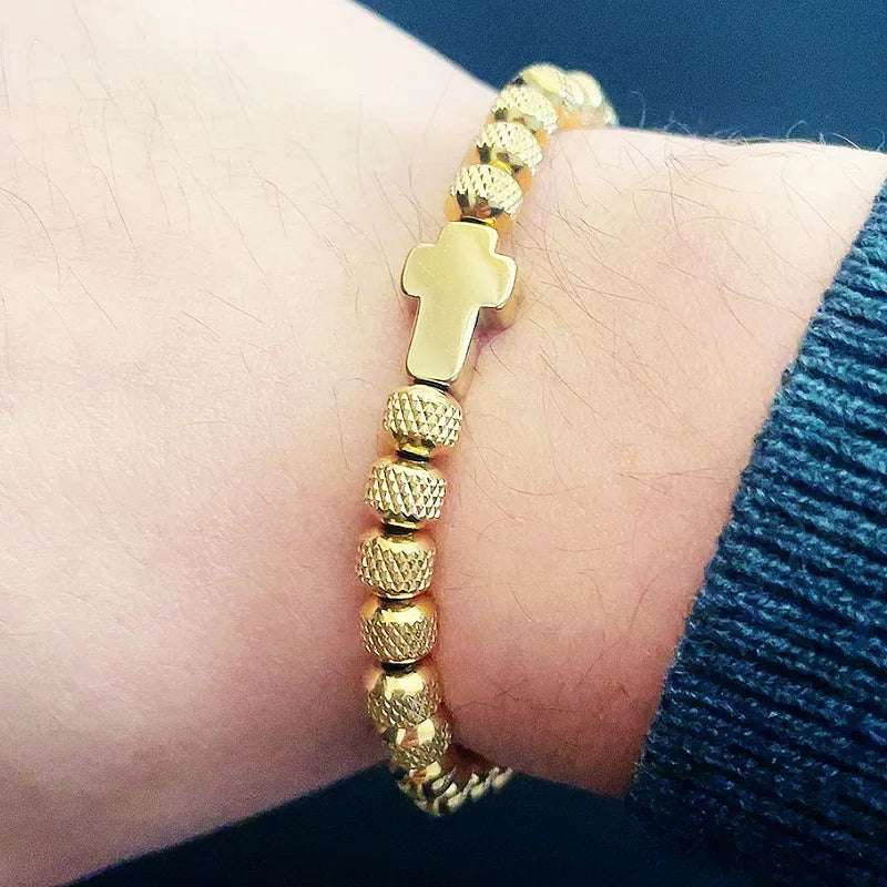 Gold bracelet with a cross charm on a wrist against a blue background