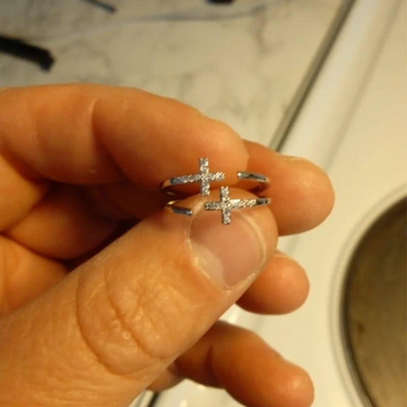 Silver cross-shaped earrings held between fingers with a blurred background