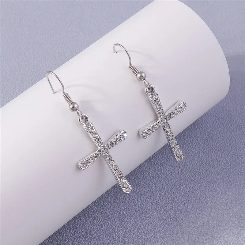 Silver cross-shaped earrings on a white cylindrical object with a light purple background