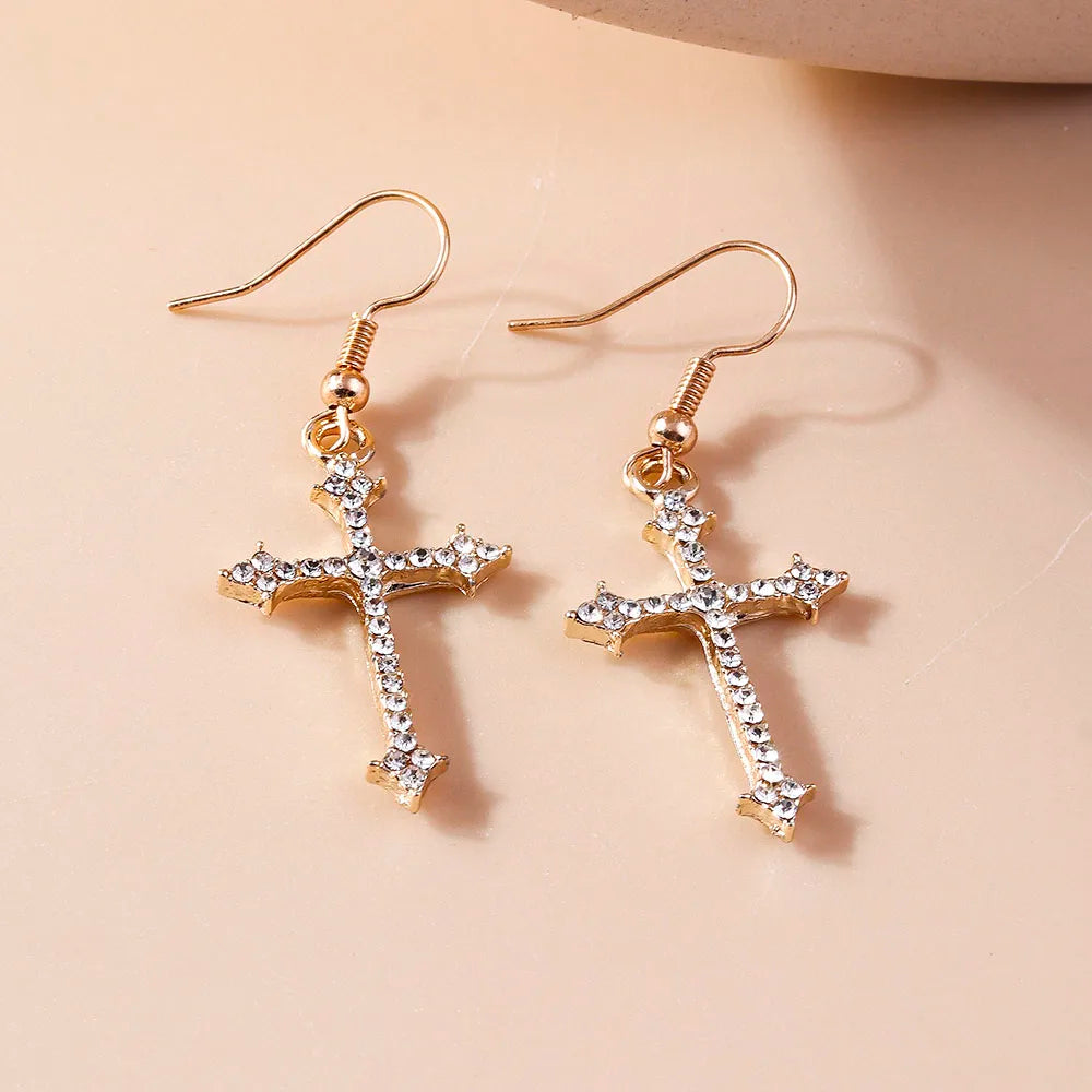 Gold cross earrings with clear stones on a beige background