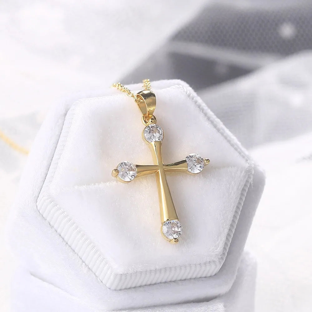 Gold cross necklace with clear stones on a white hexagonal jewelry box