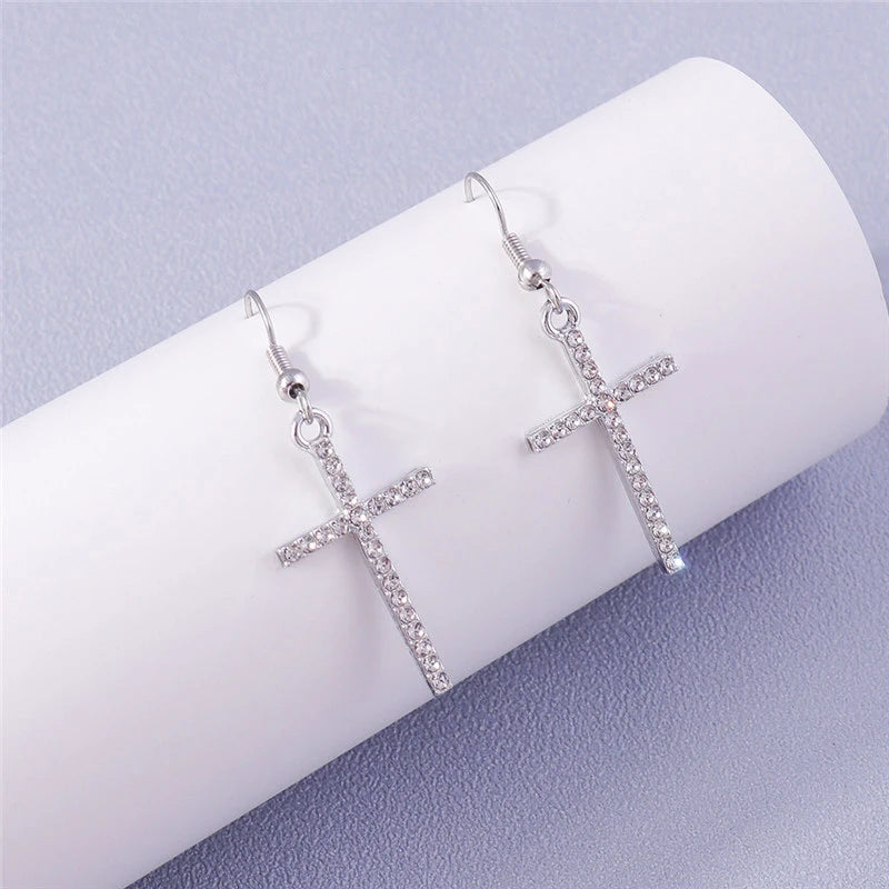 Silver cross-shaped earrings on a white cushion with a light purple background