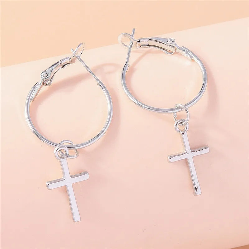 Silver hoop earrings with cross charms on a beige background