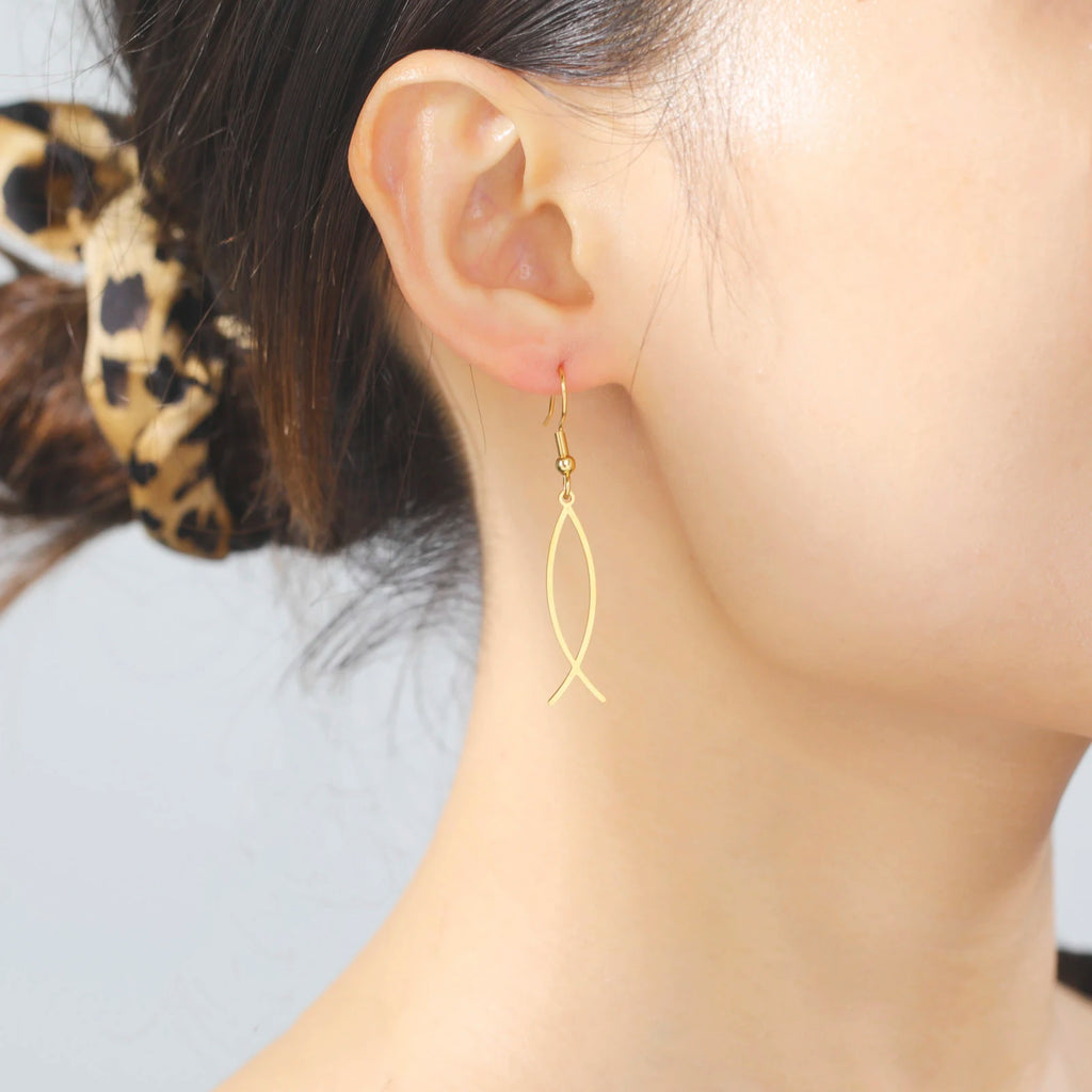 Gold fish-shaped earrings worn by a person with a blurred background