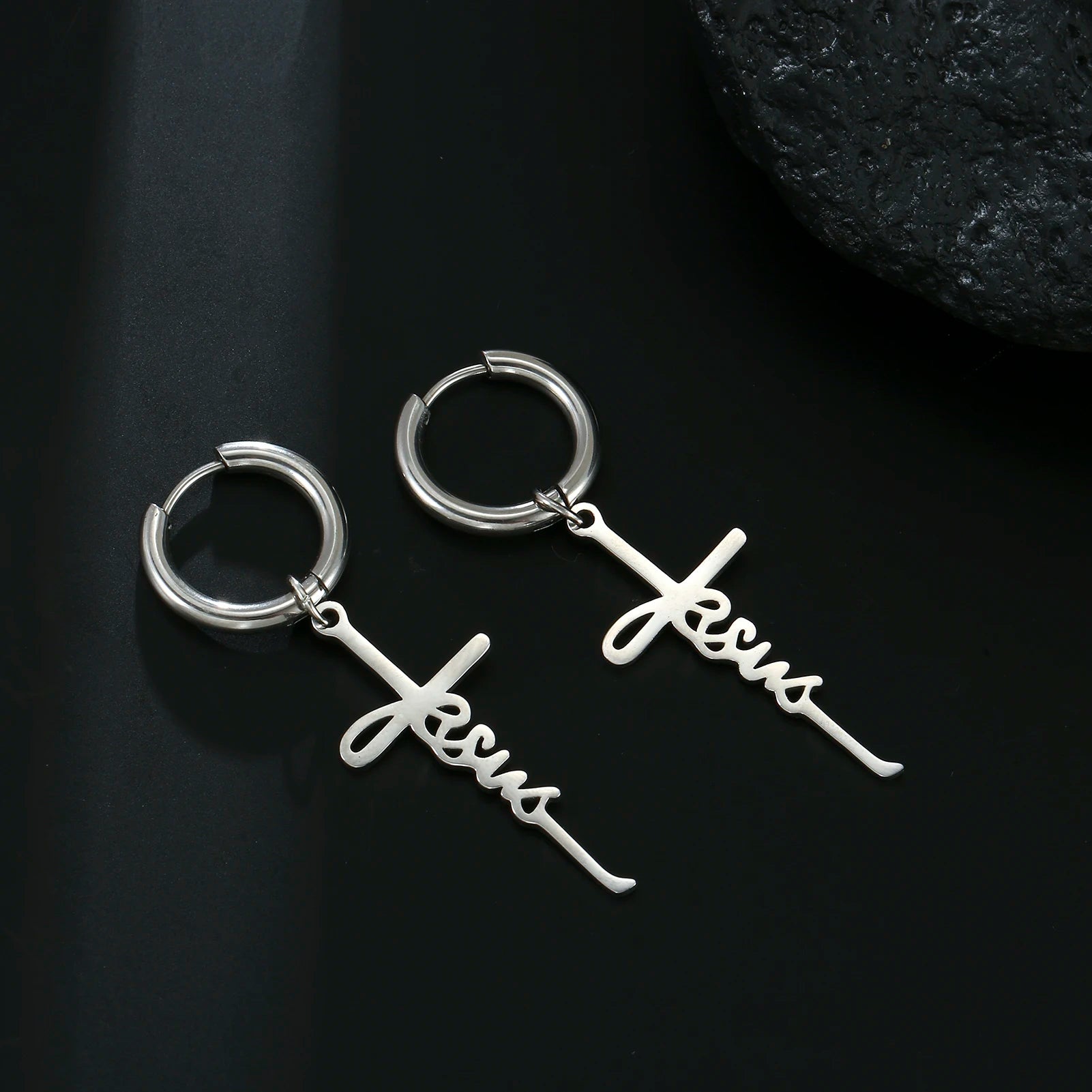 Silver hoop earrings with 'Jesus' script on a white fabric background
