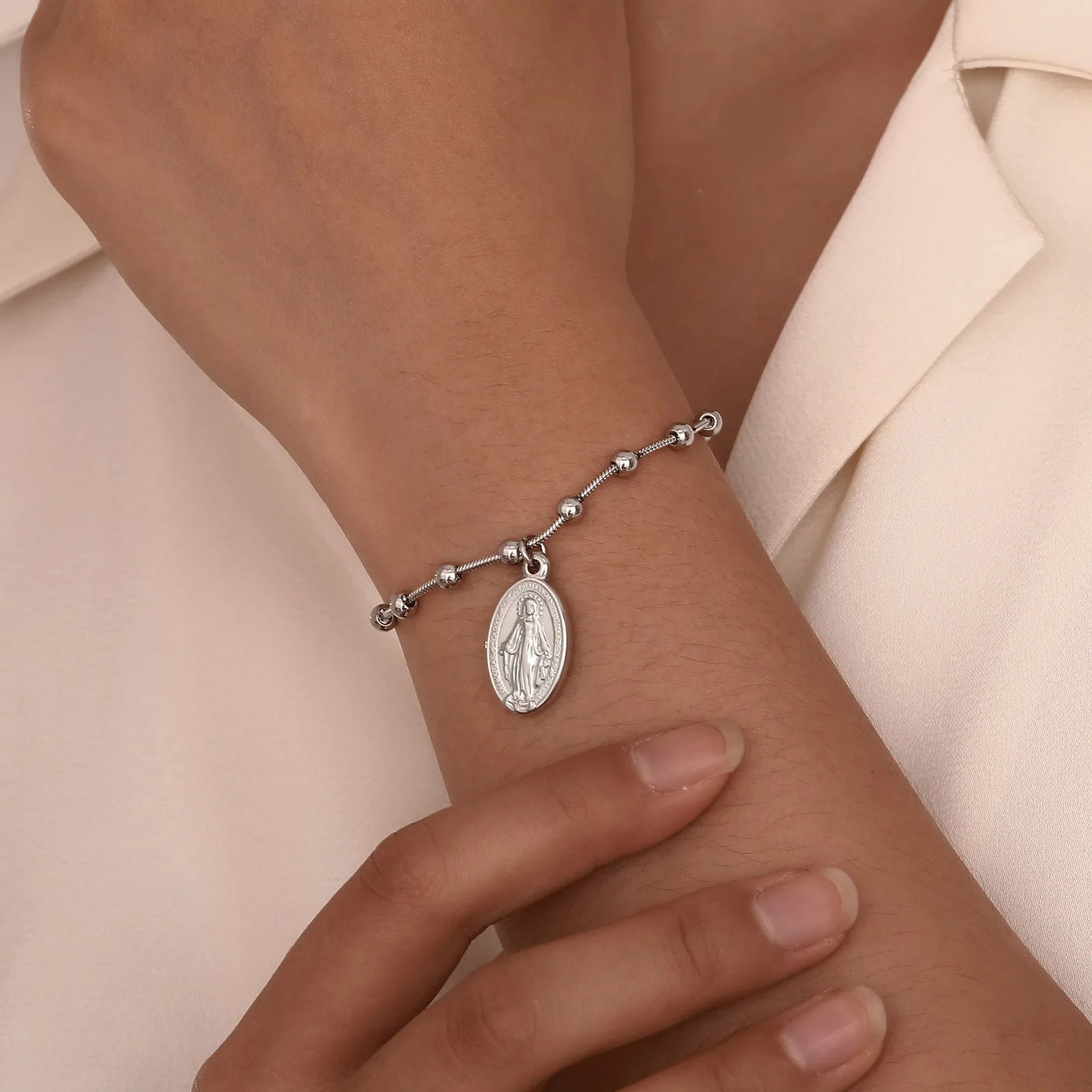 Silver bracelet with a pendant on a wrist against a neutral background