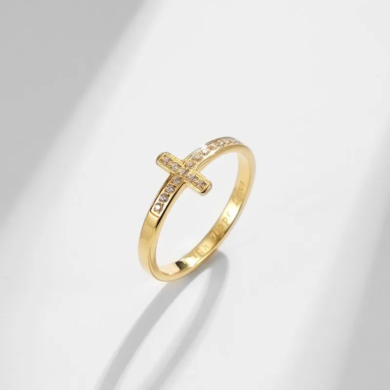 Gold ring with a cross design on a light gray background