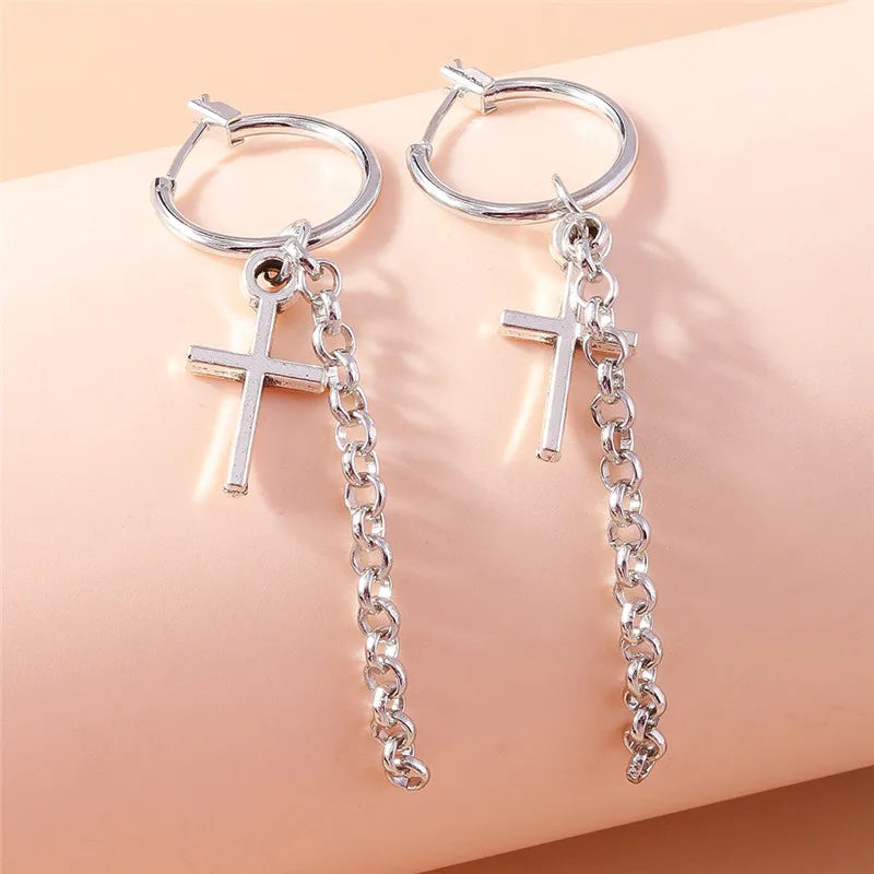 Silver hoop earrings with chain extensions and cross pendants on a beige background