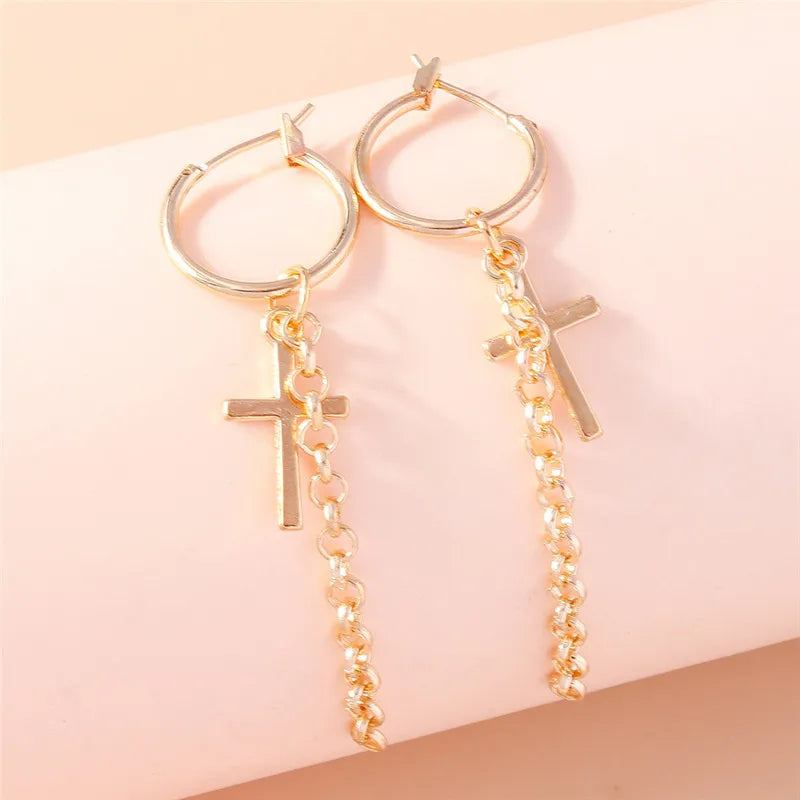 Gold hoop earrings with cross and beaded charms on a pink background