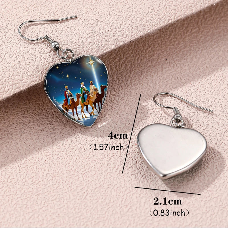 Heart-shaped earrings with nativity scene design and measurements on a pink background