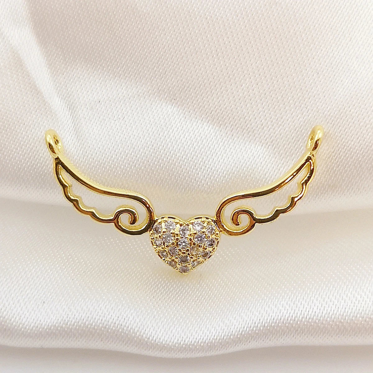 Gold winged heart-shaped earring on a light pink fabric background
