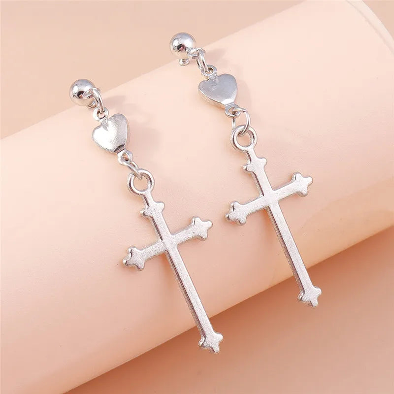 Silver cross earrings with heart charms on a beige background
