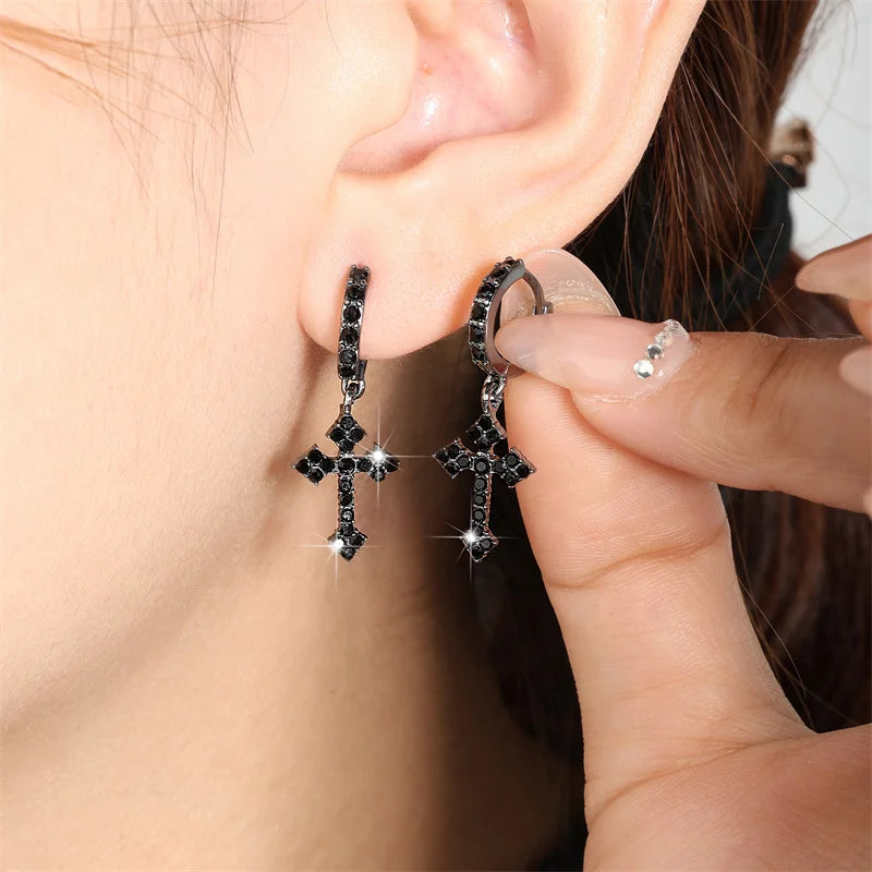Person wearing black cross earrings with clear stones.