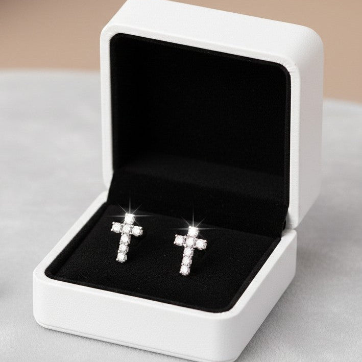 Silver cross earrings in a white jewelry box on a light gray surface.