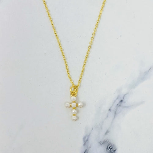 Gold necklace with a cross pendant featuring three pearls on a marble surface