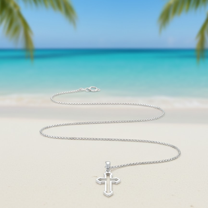 Silver cross necklace on a sandy beach with palm trees and blue sky in the background