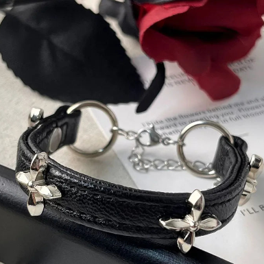Black leather bracelet with silver studs on a surface with a red flower and black glove in the background.