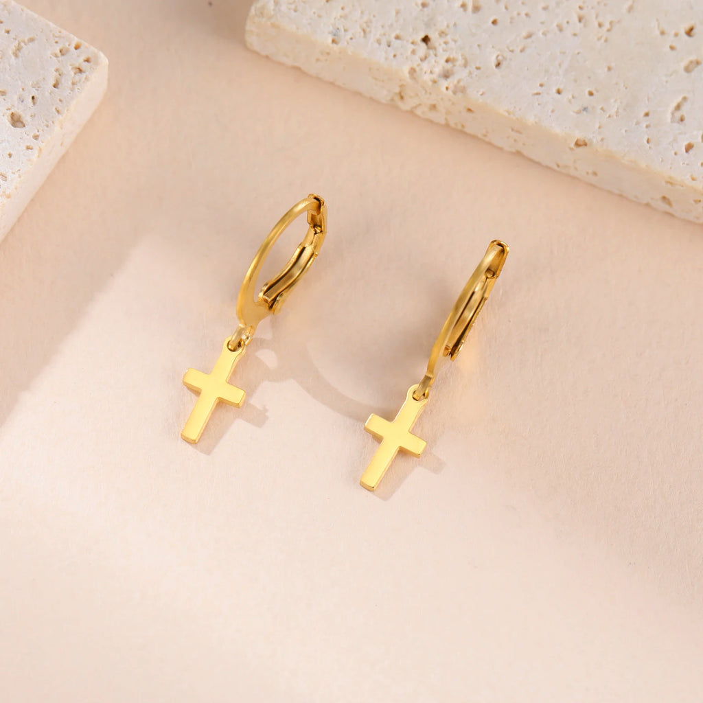 Gold hoop earrings with cross pendants on a beige surface