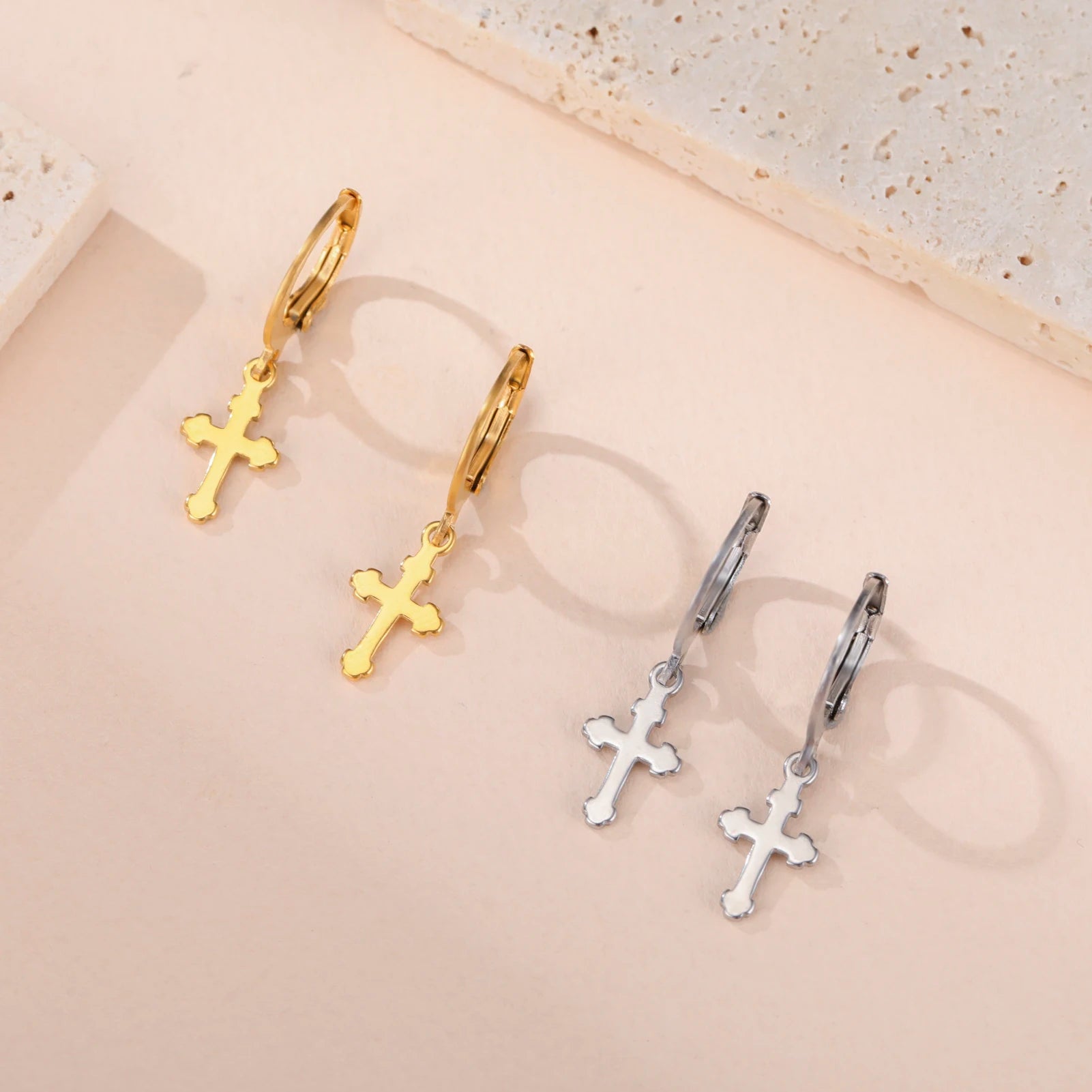 Gold and silver cross earrings on a beige background