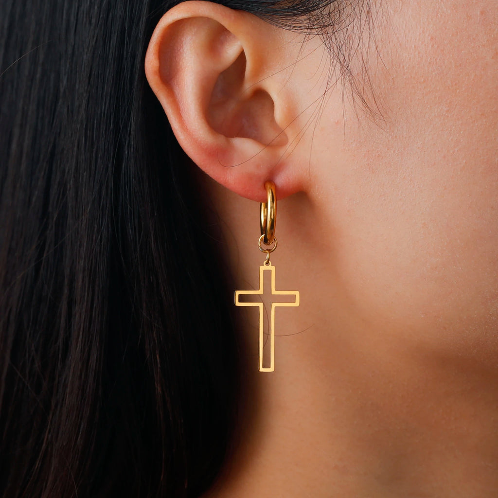 Gold cross earring worn by a person with dark hair.