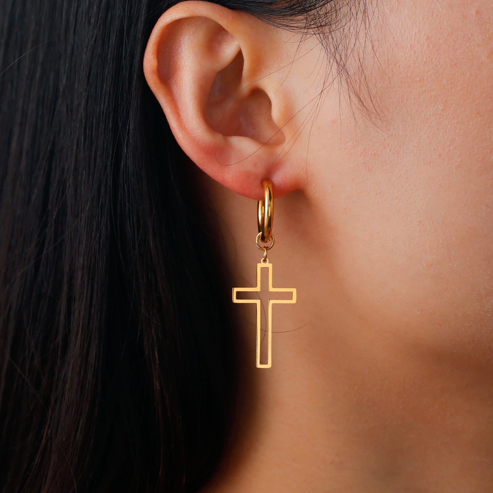 Gold cross earring worn by a person with dark hair.