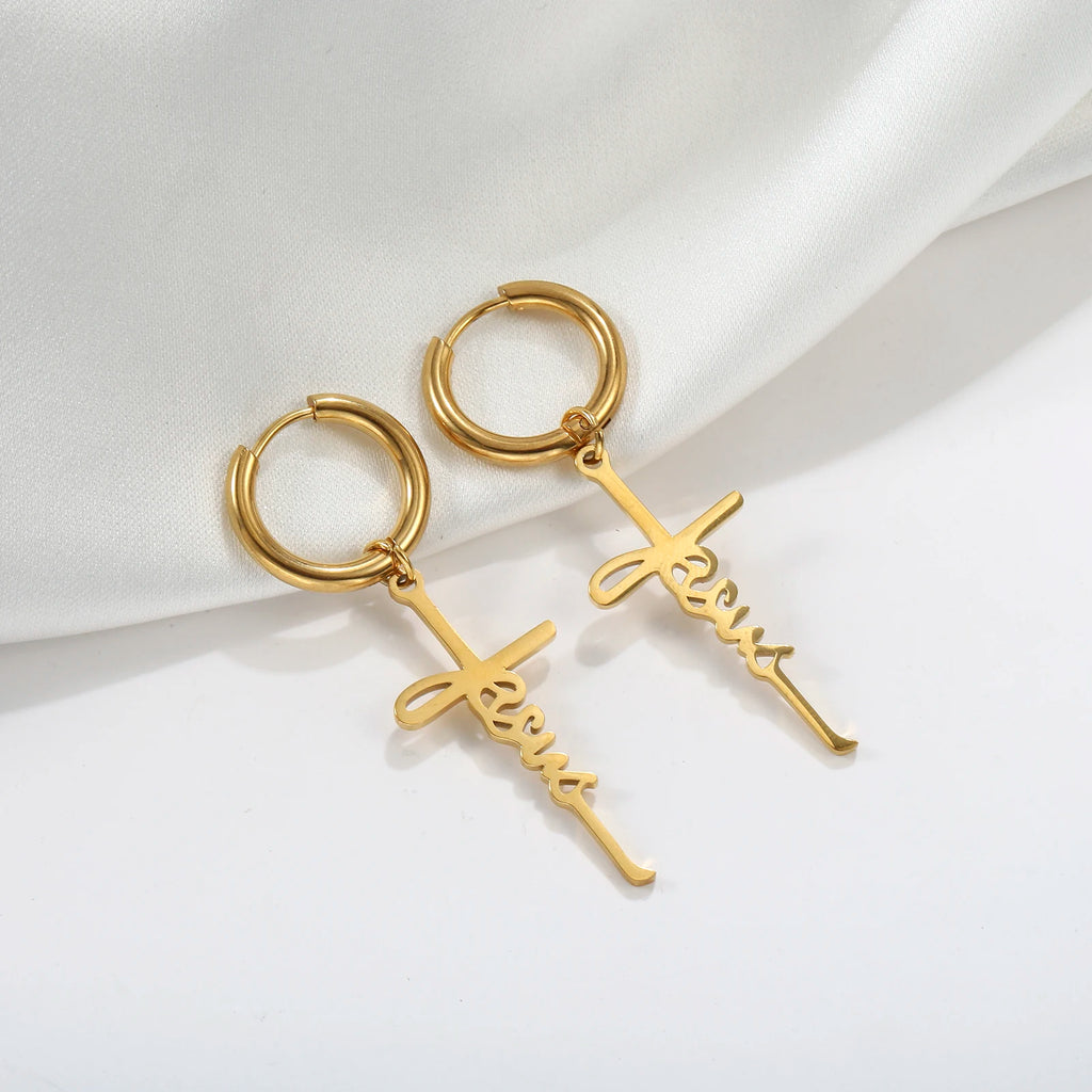 Gold hoop earrings with 'Jesus' script on a white fabric background