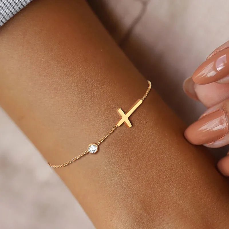 Gold bracelet with a cross and small gemstone on a wrist