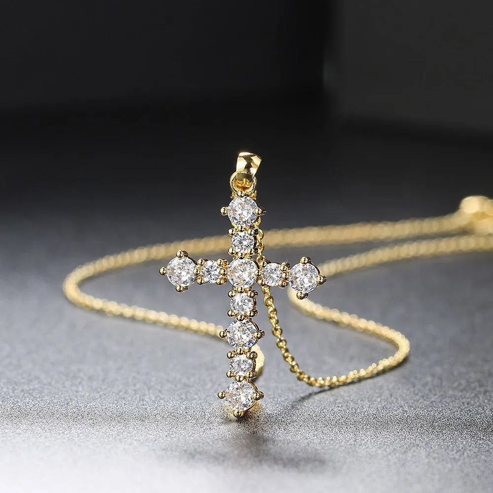 Gold cross pendant necklace with clear stones on a dark background