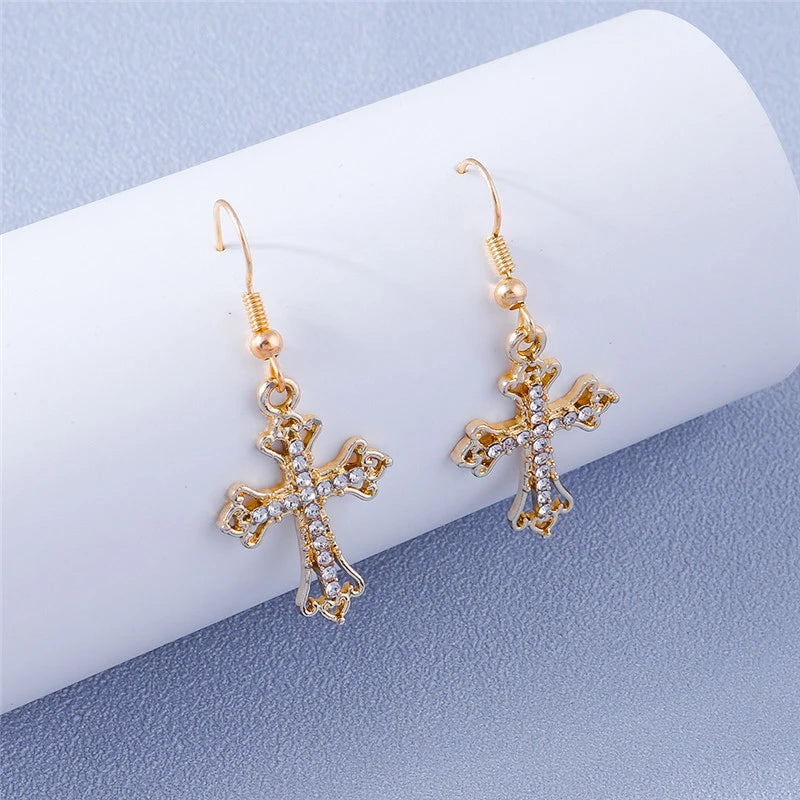 Gold cross earrings with clear stones on a white and blue gradient background