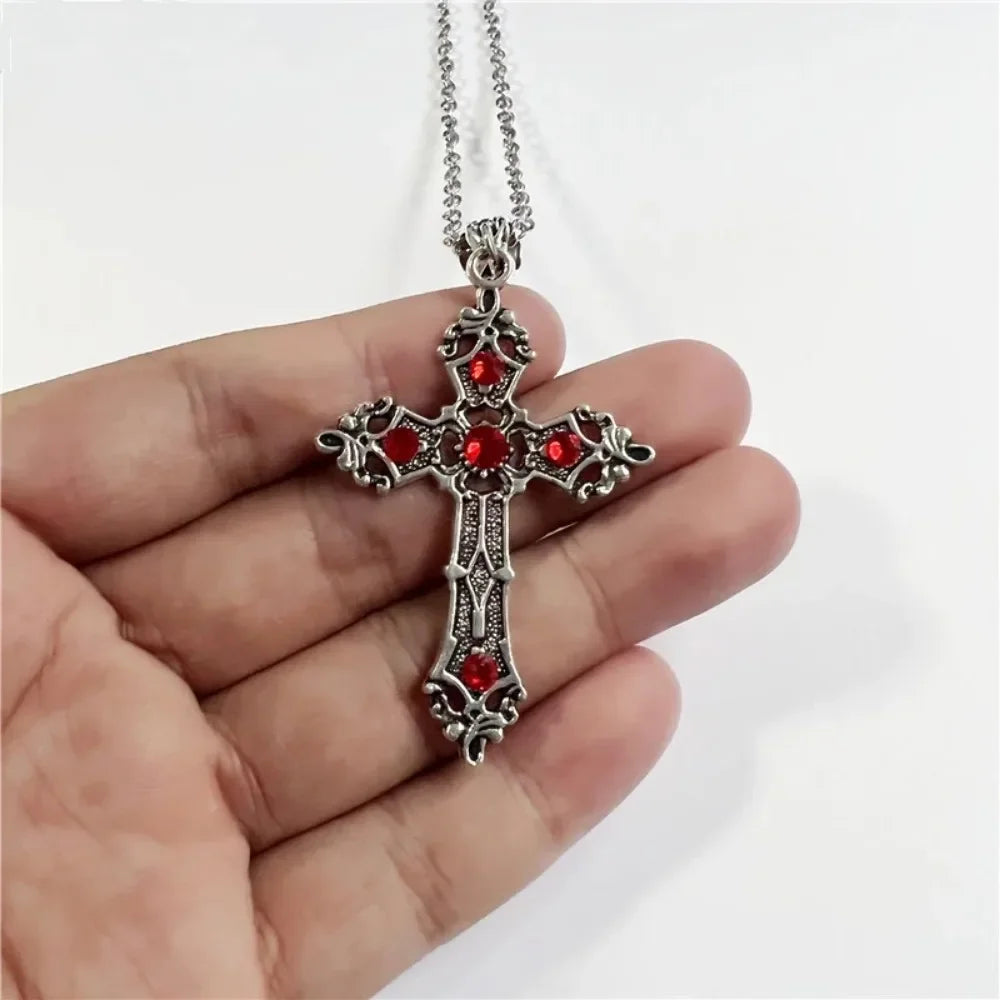Silver cross pendant with red stones held in a hand against a white background