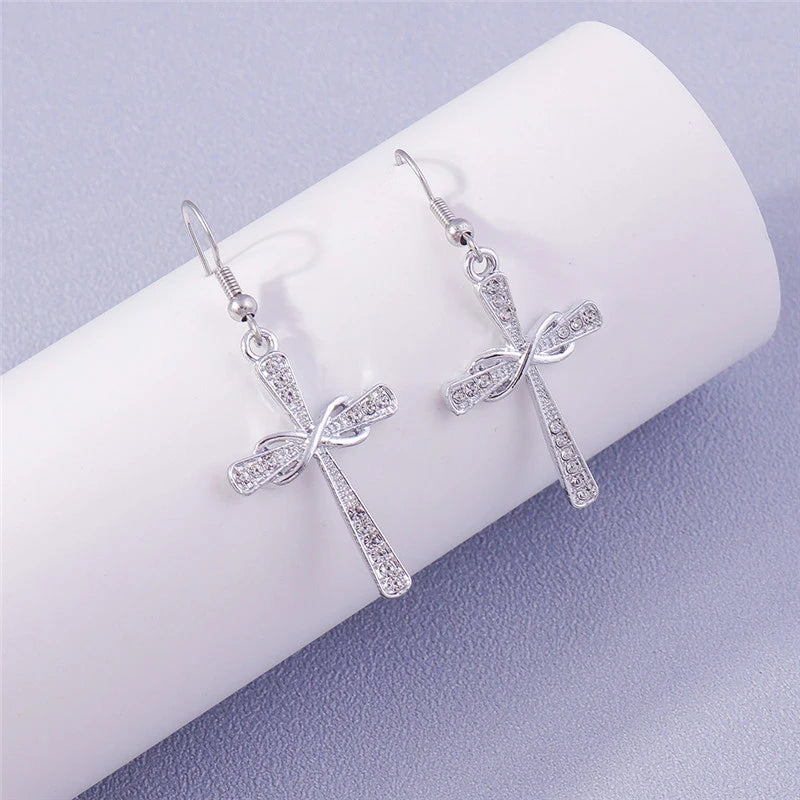 Silver cross-shaped earrings with bow details on a white surface.