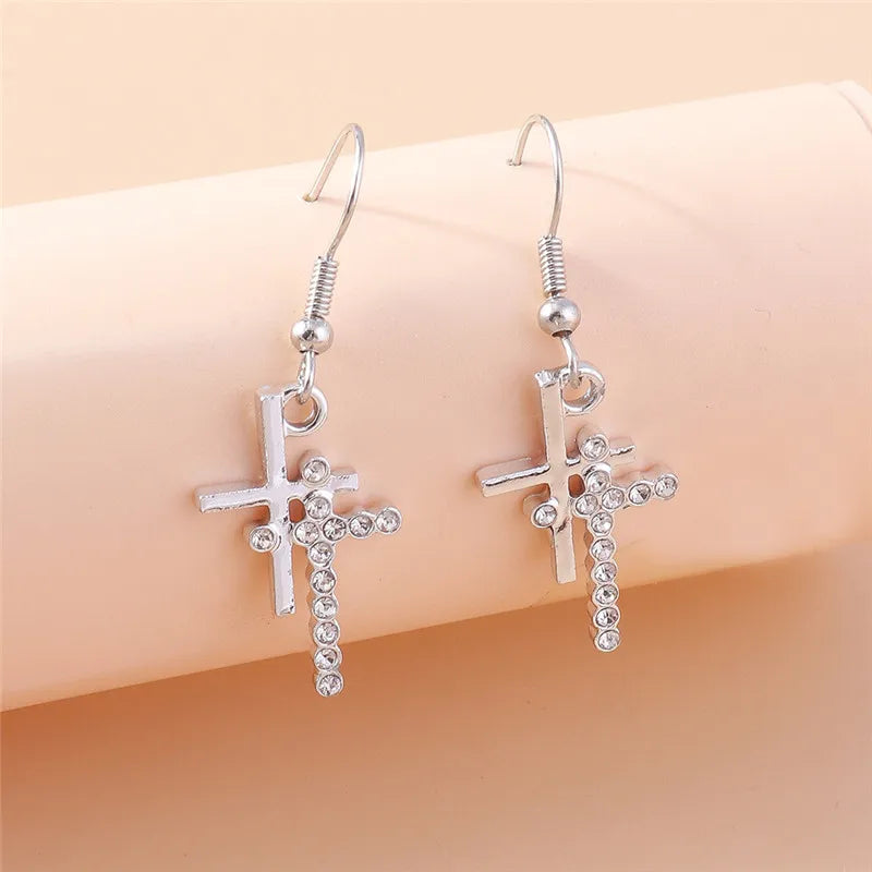 Silver cross earrings with rhinestones on a beige background