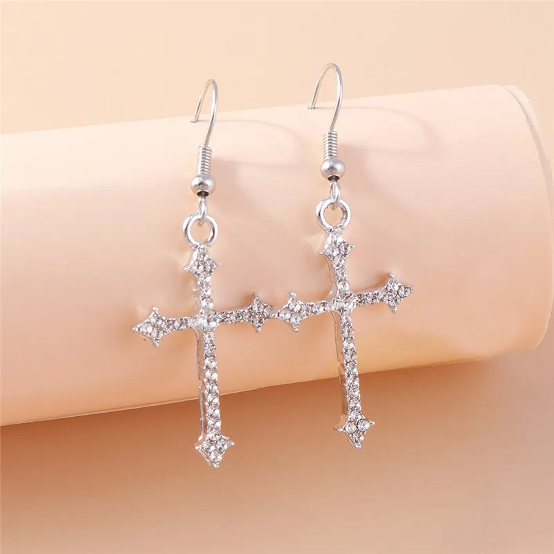 Silver cross earrings with clear stones on a beige background