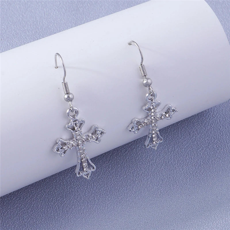 Silver cross earrings on a white cylindrical object with a light purple background
