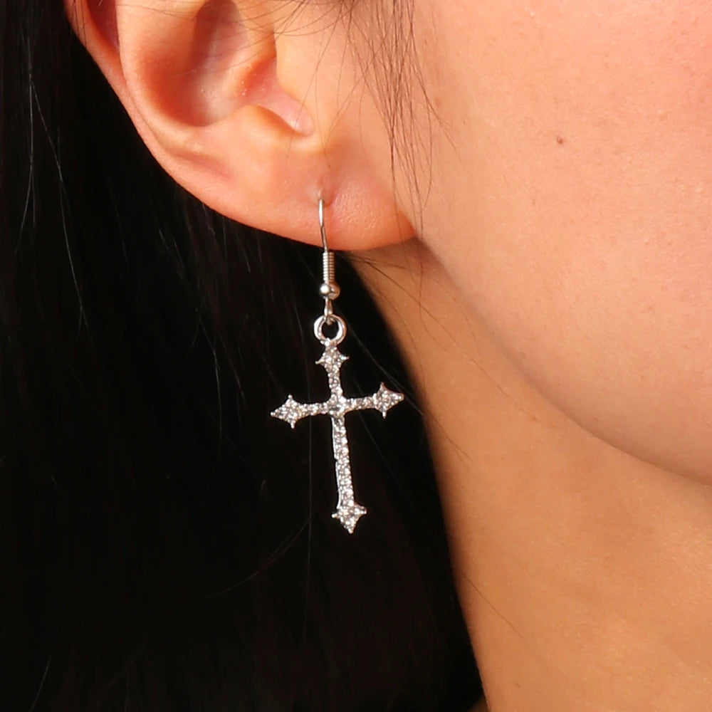 Silver cross earring worn by a person with a black background