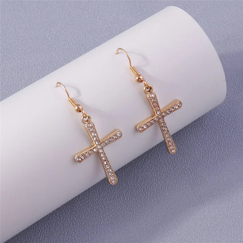 Gold cross earrings on a white cylindrical stand with a gray background